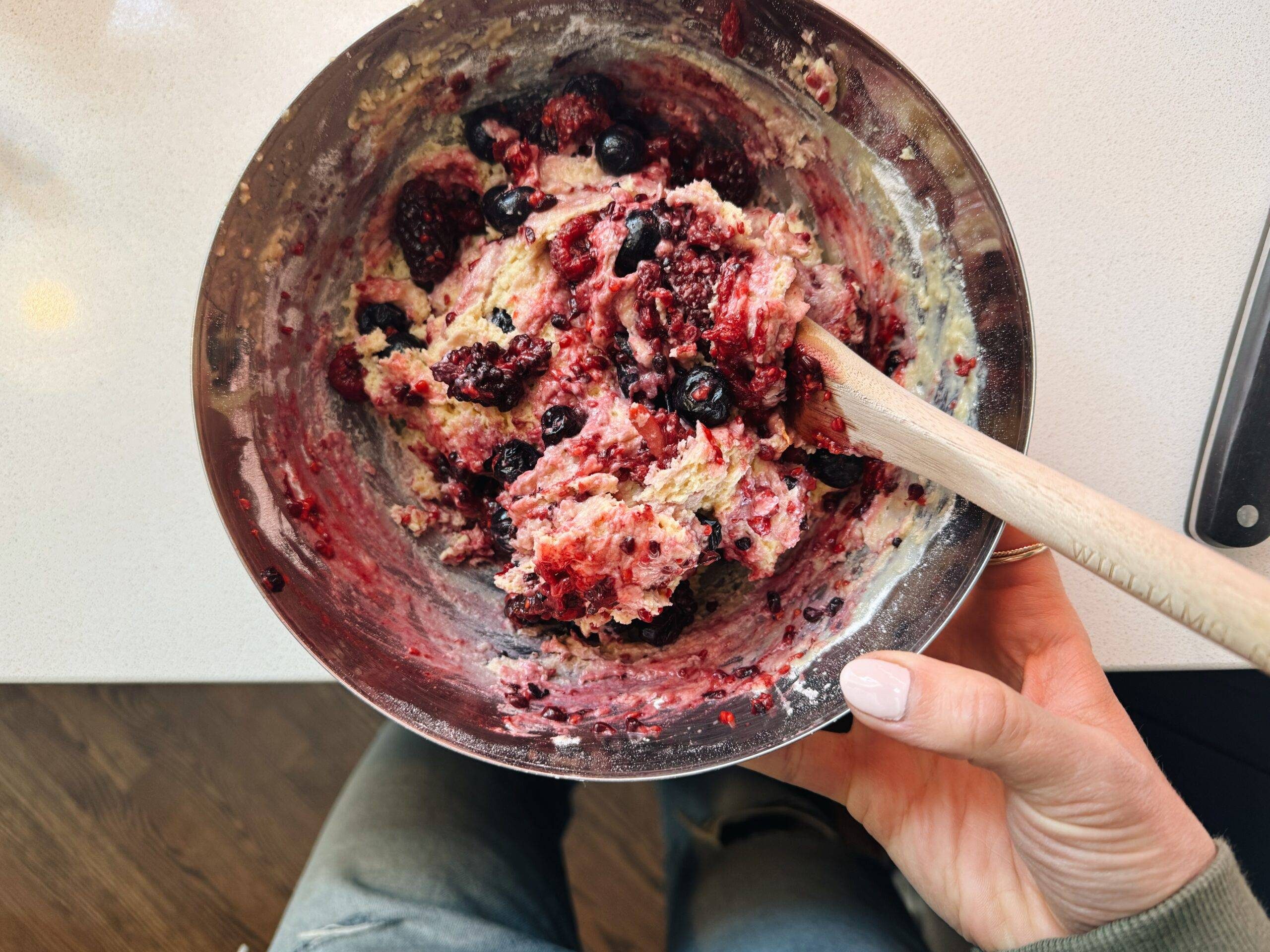 Mixing berries into batter in a bowl.