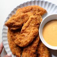 Chicken tenders on a plate with sauce on the side.