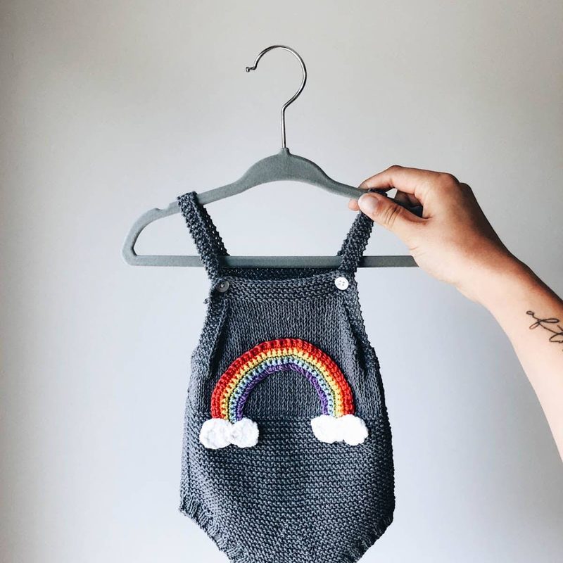 A hand holding a hanger and a baby sweater is hanging on it.