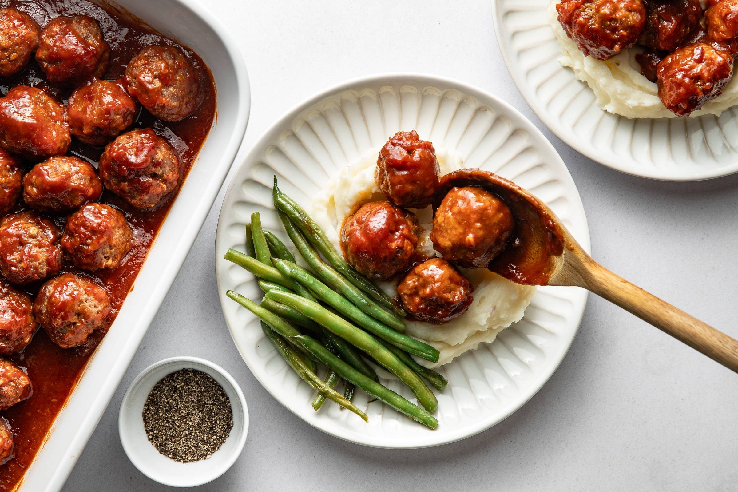 Spooning bbq meatballs over mashed potatoes with green beans on the side.