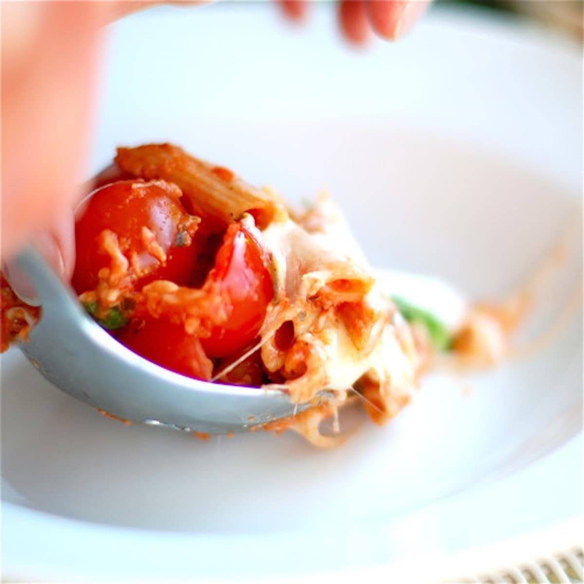 Vegetarian caprese penne pasta with sweet cherry tomatoes, mozzarella, and fresh basil on a spoon.