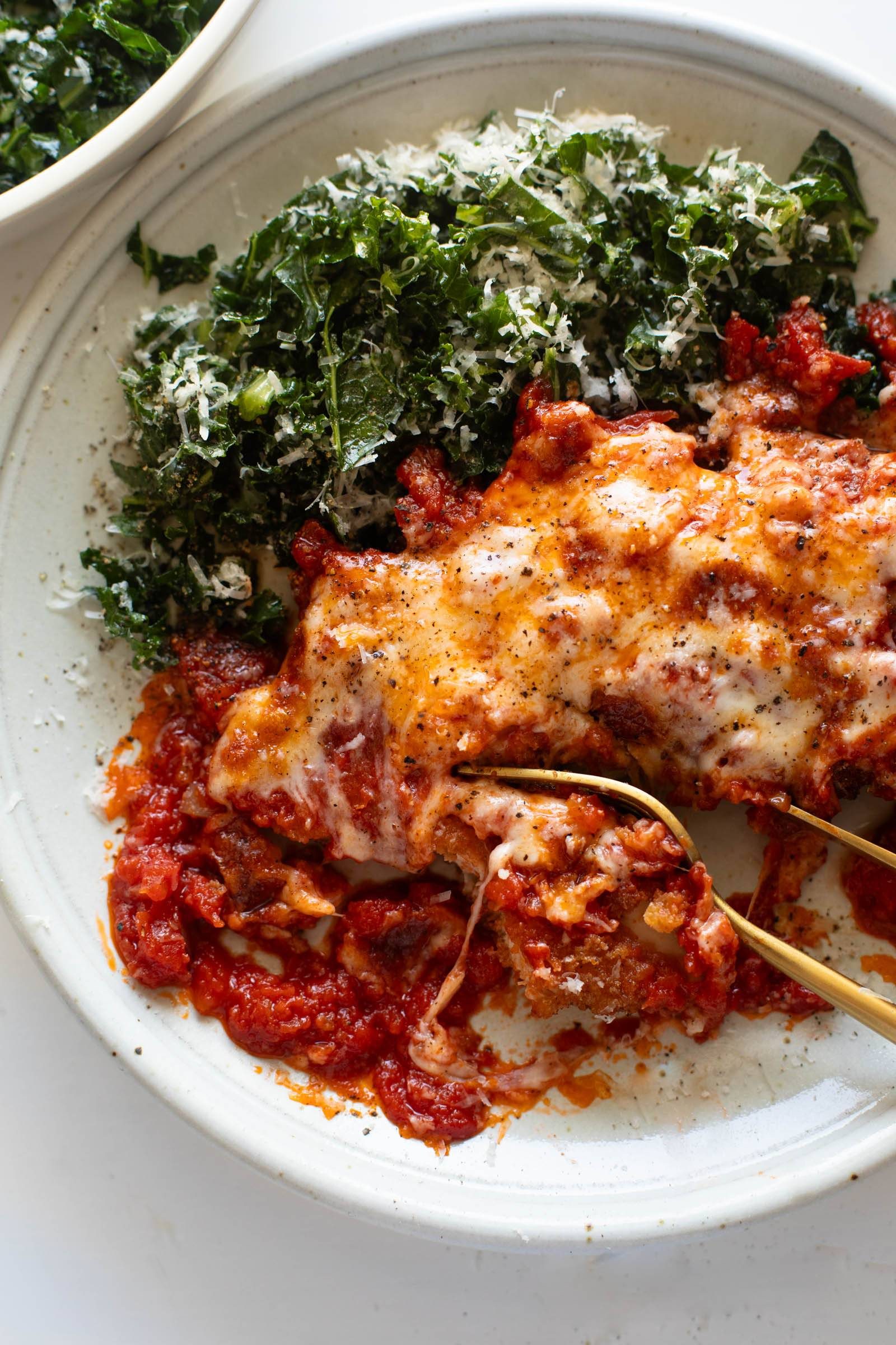 Chicken parmesan on a plate with kale salad.