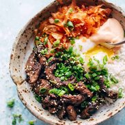 Korean beef along with carrot, onion and spicy mayo in a bowl with a spoon.