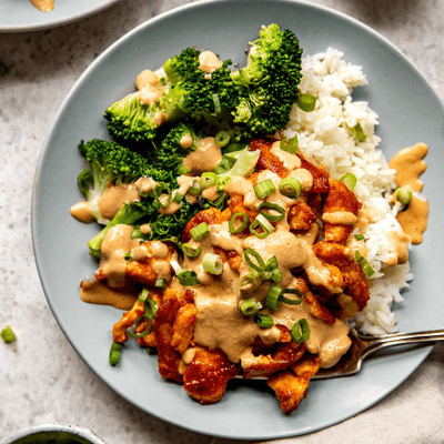 Red curry chicken stir fry in a bowl with broccoli, rice, and cashew sauce.
