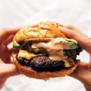 Hands holding a juicy smash burger with sauce.
