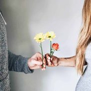 One man and a woman is holding flowers in their hands and holding hands together.